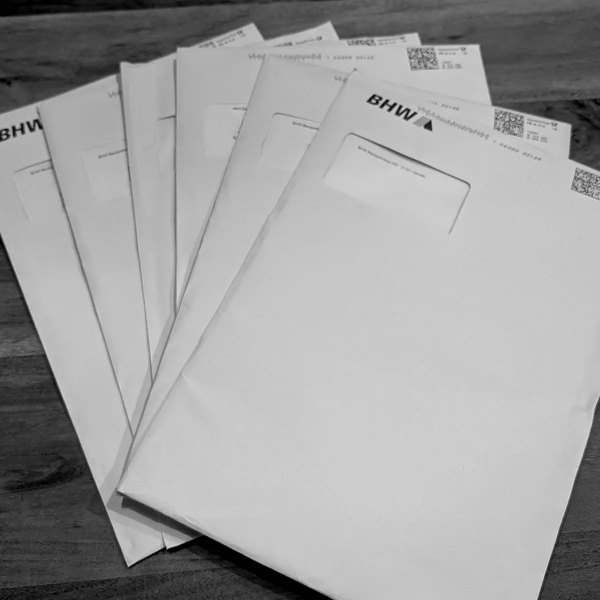 Bausparbürokratie in Papierform – sechs Umschläge vom BHW, wie ein Fächer ausgebreitet auf Holztisch.