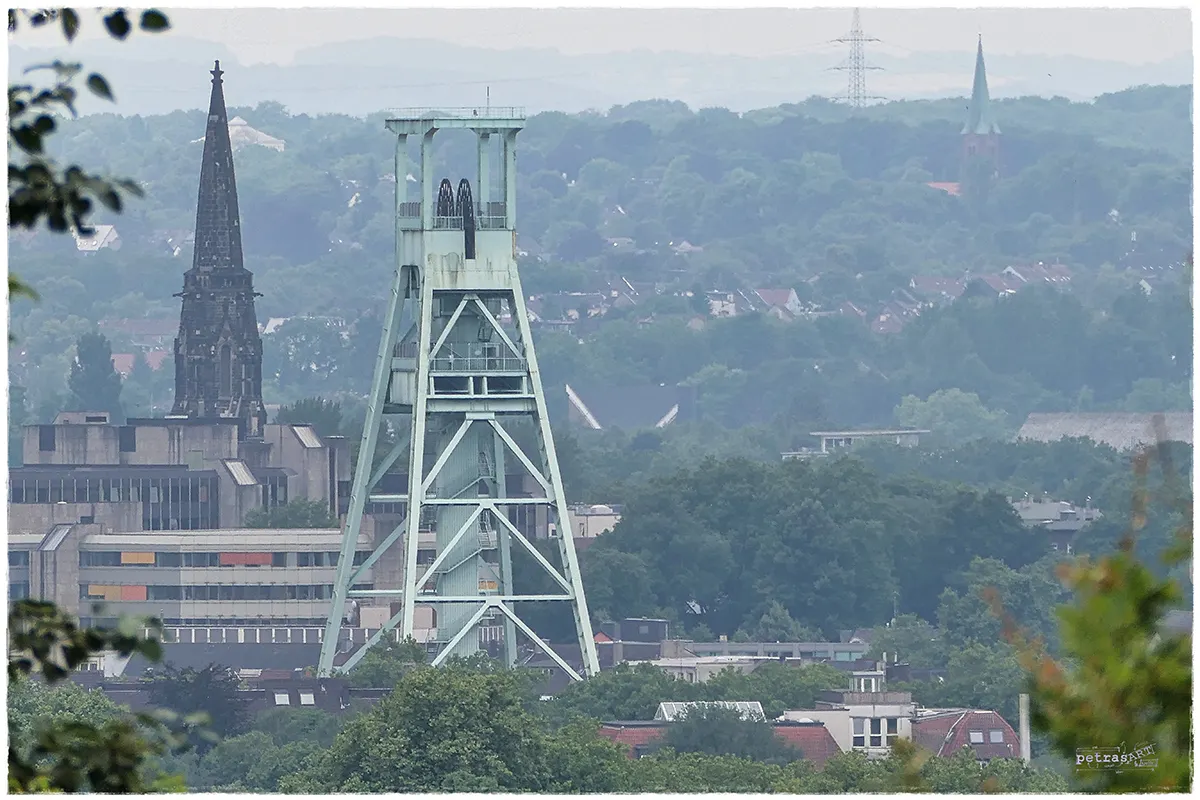 Fotografie eines Förderturms mit städtischem Hintergrund, aufgenommen mit Superzoom aus der Ferne.
