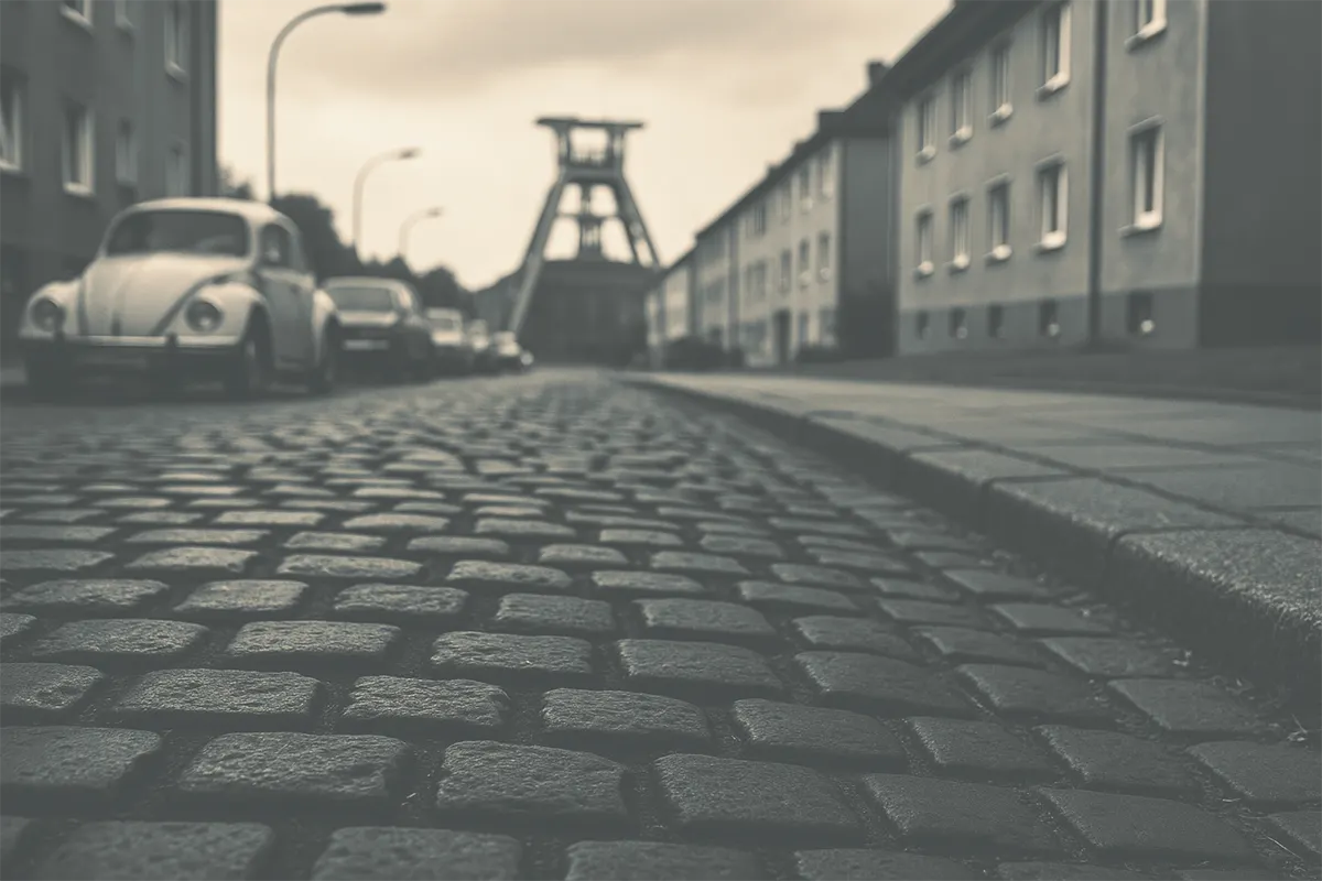 Kopfsteinpflaster-Straße in Bochum-Riemke mit VW Käfer und Zechenturm, nachgestellte Szene im Stil der 1970er Jahre.
