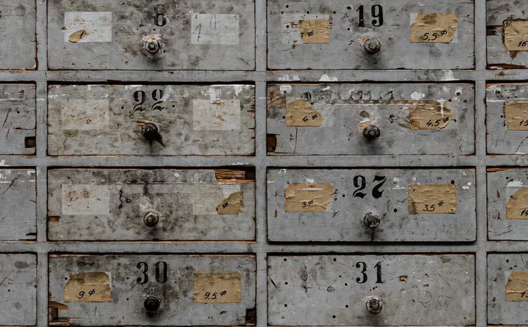 Ausschnitt eines alten Schubladenschranks mit mehreren nummerierten Fächern – Symbol für das Sortieren von Menschen, Meinungen und Kategorien.