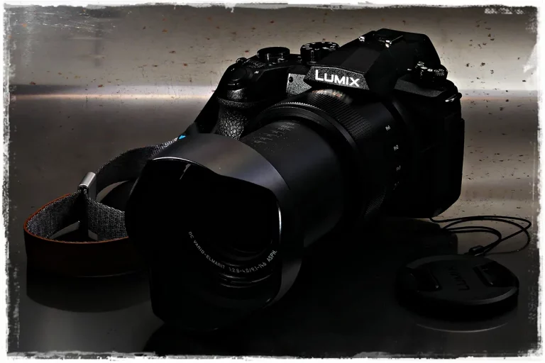 Panasonic FZ1000 II Superzoom-Bridgekamera mit Gegenlichtblende, frontal aufgenommen. Seitenansicht der Panasonic FZ1000 II Kamera mit Handgelenks-Trageriemen.