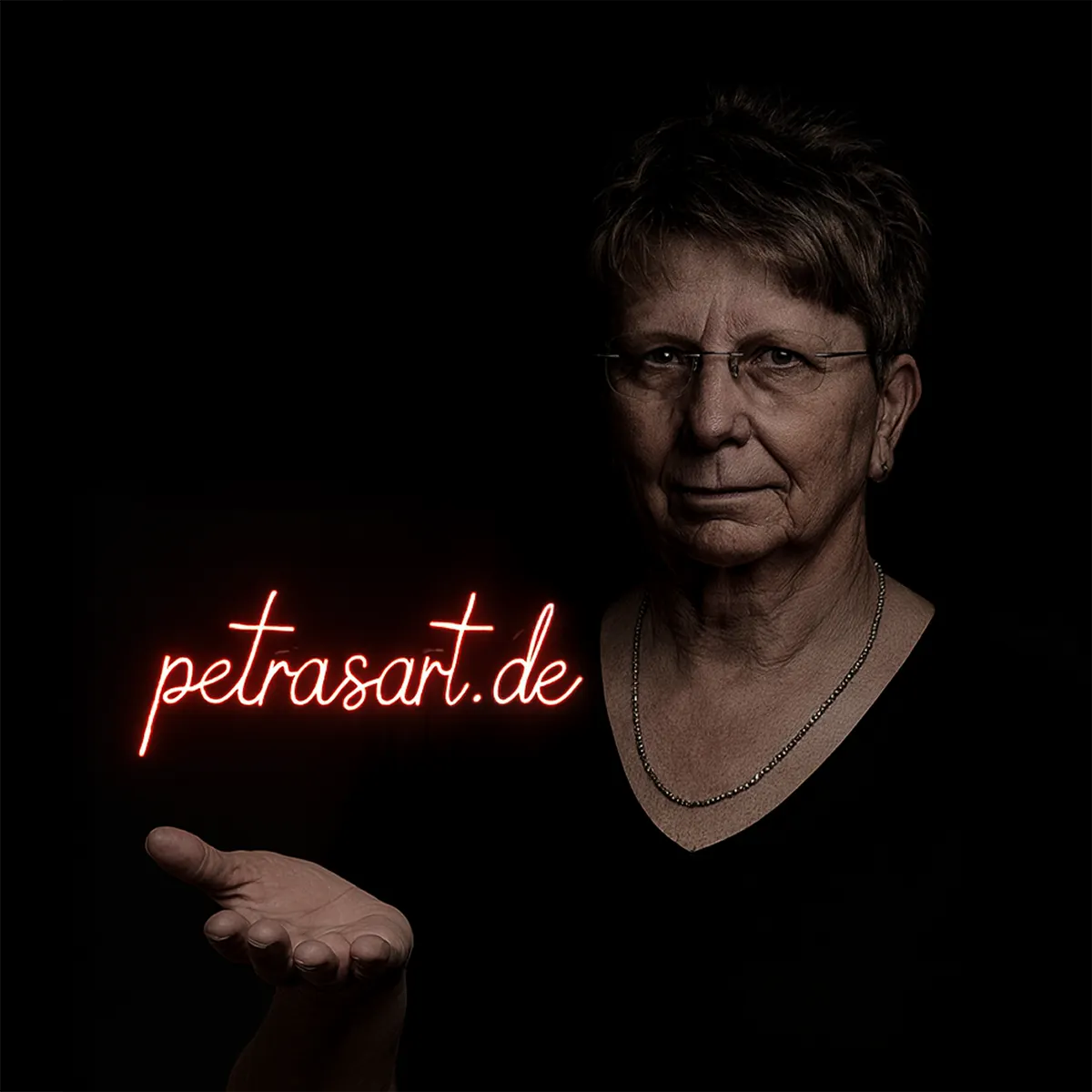 Petra mit kurzem blonden Haar, Brille, schwarzem Shirt vor dunklem Hintergrund. In der rechten Hand schwebt der rote Neon-Schriftzug petrasart.de